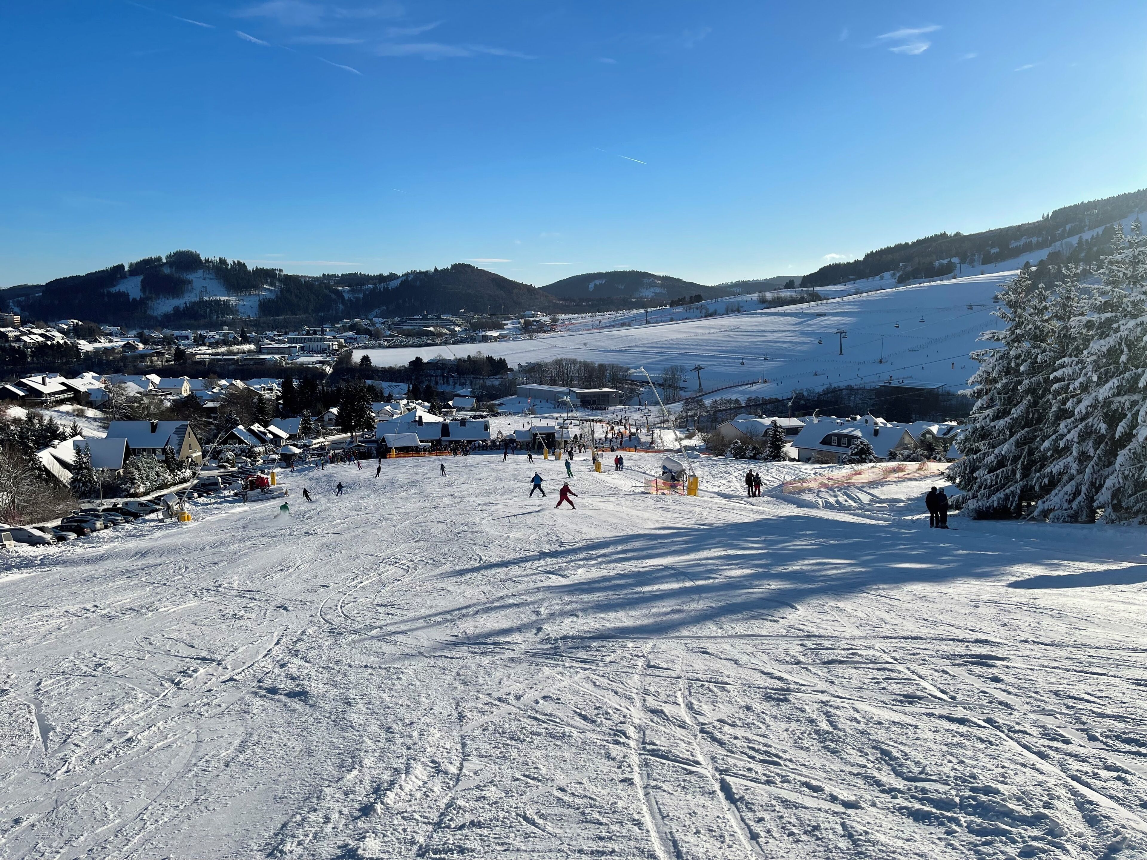 A ski resort with a ski lift, snow-covered slopes, and buildings in the background.