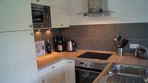A modern kitchen with white cabinets, a built-in oven, a microwave, a coffee maker, and a stainless steel sink. - Apartment Ritzhagen **** (Willingen (Upland))