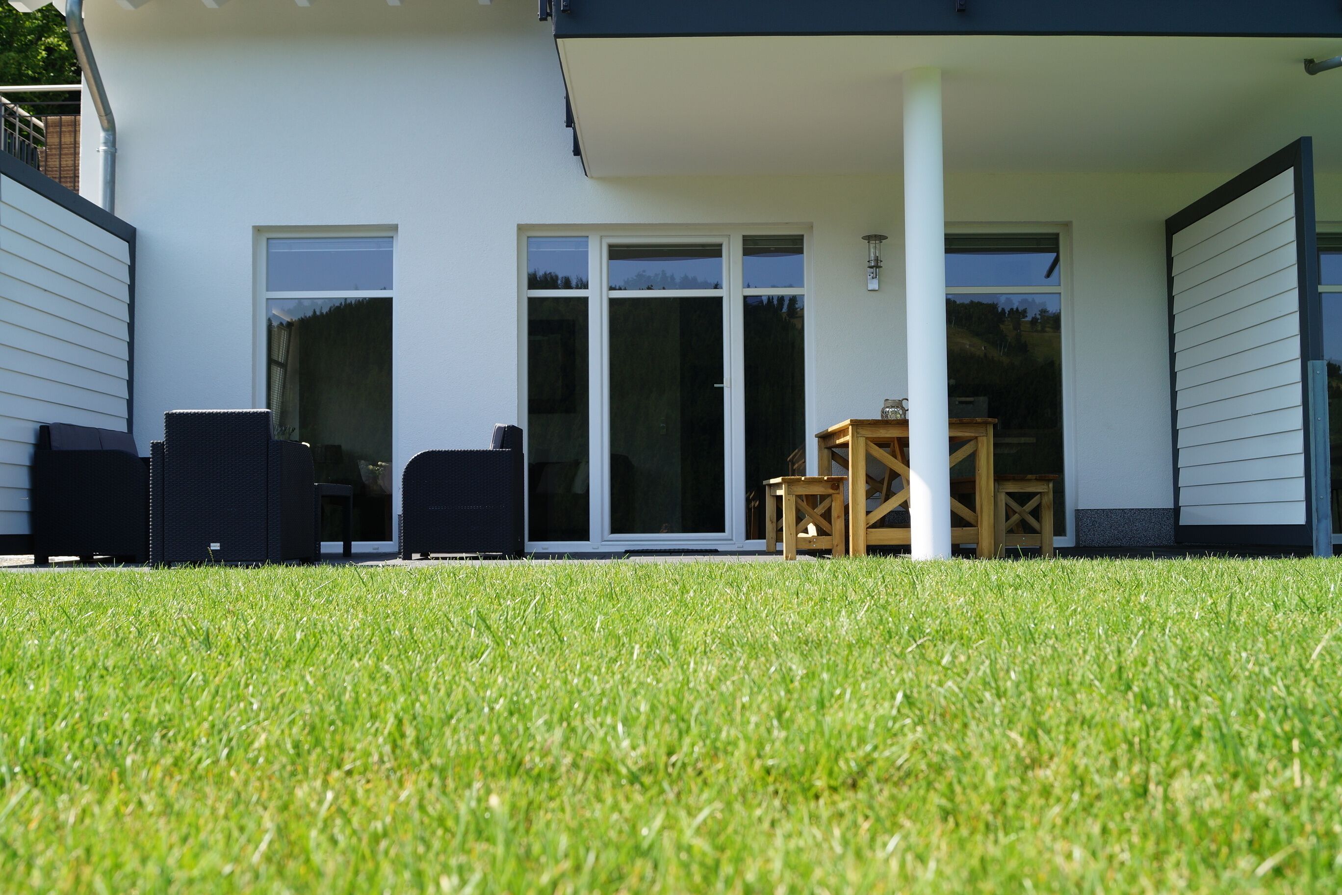 A modern house with a covered patio, a lawn, and a sliding glass door leading to an interior space.