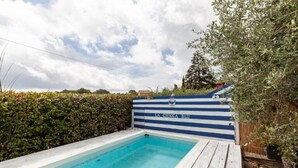 Une piscine dont le mur est décoré de rayures bleues et blanches, entourée de verdure.