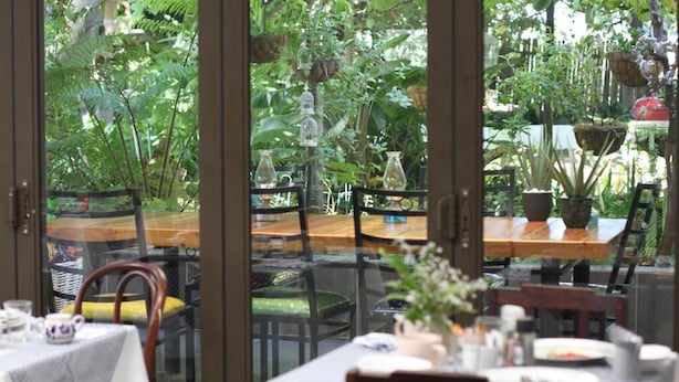 An indoor dining area with tables and chairs, surrounded by lush greenery and potted plants. - Rouana Guest Farm (Stellenbosch)