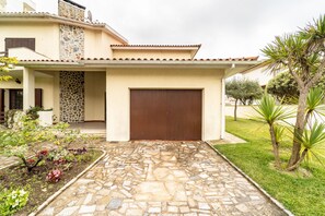 A house with a stone-tiled entrance, a brown garage door, and a garden with various plants. - Amorosa Villa, 500m from the beach by House and People (Viana do Castelo)