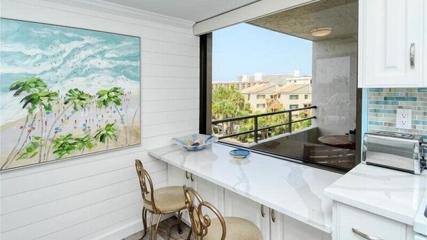 A modern kitchen with a large window, white cabinetry, and a dining area with two chairs. - Anchorage 404 (Siesta Key)