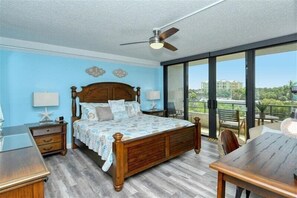 Une chambre à coucher avec un lit en bois, des tables de chevet, un bureau et un balcon avec vue.
