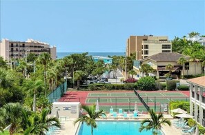 A hotel with a swimming pool, tennis court, and palm trees.