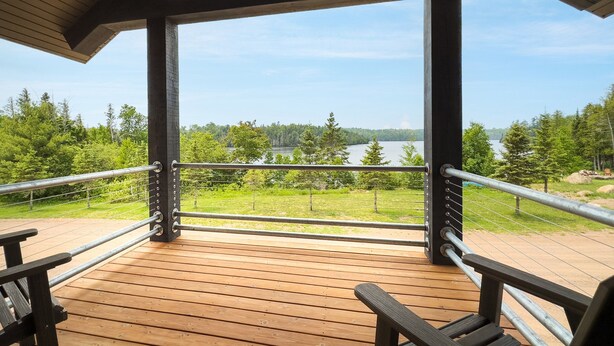 Una terraza de madera con barandillas de metal que da a un lago y un bosque.