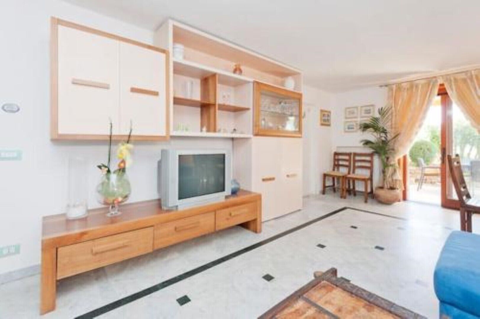 A living room with a TV, wooden furniture, and a dining area with chairs and a table.