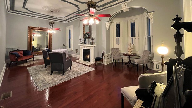 Een ruime woonkamer met een open haard, elegante meubels en decoratieve plafondlijsten.