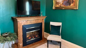 Ein Wohnzimmer mit Kamin, Fernseher und einem gerahmten Gemälde an der Wand.
