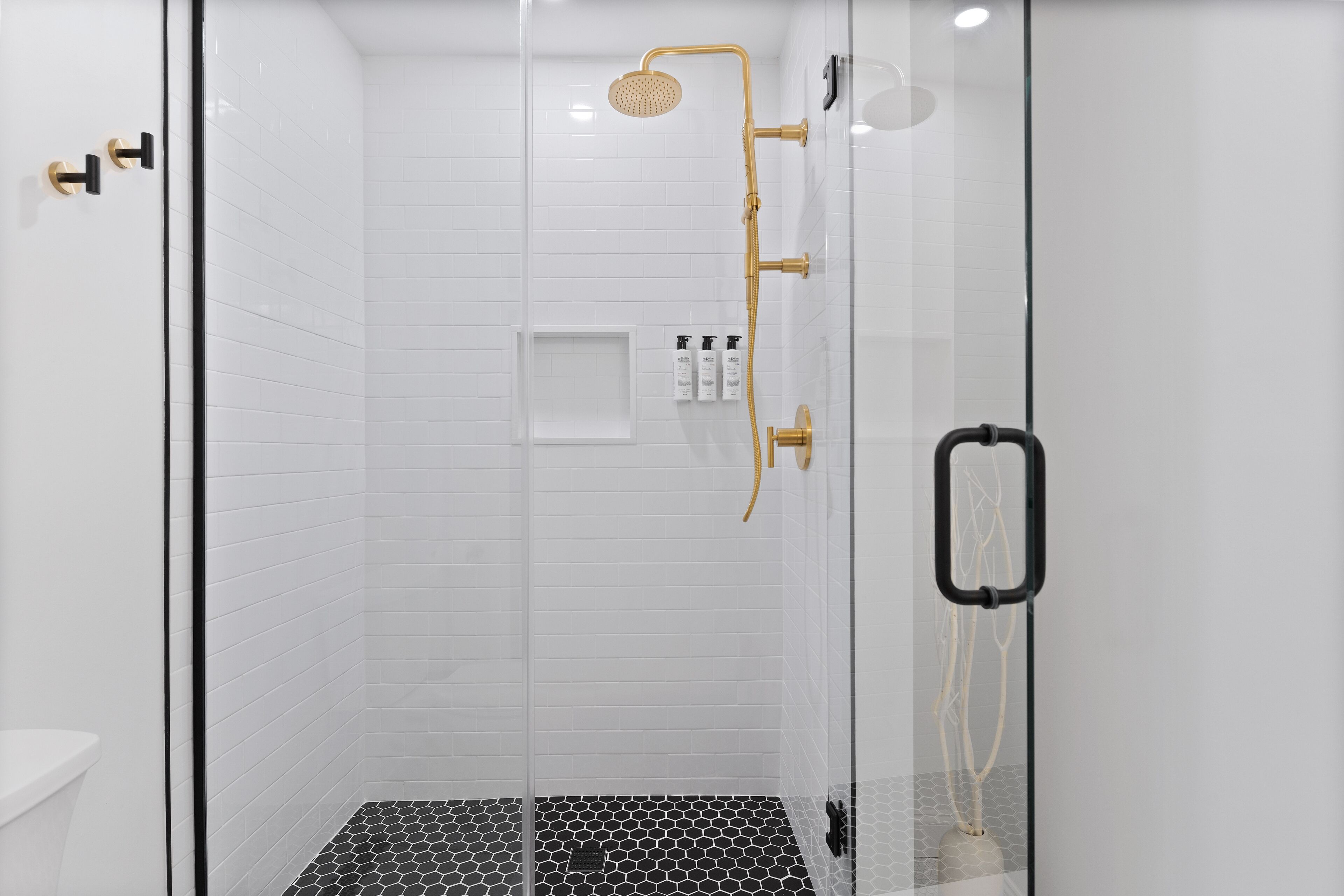 A glass-enclosed shower with a gold showerhead and black handles.