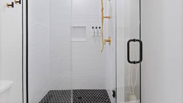 A glass-enclosed shower with a gold showerhead and black handles.