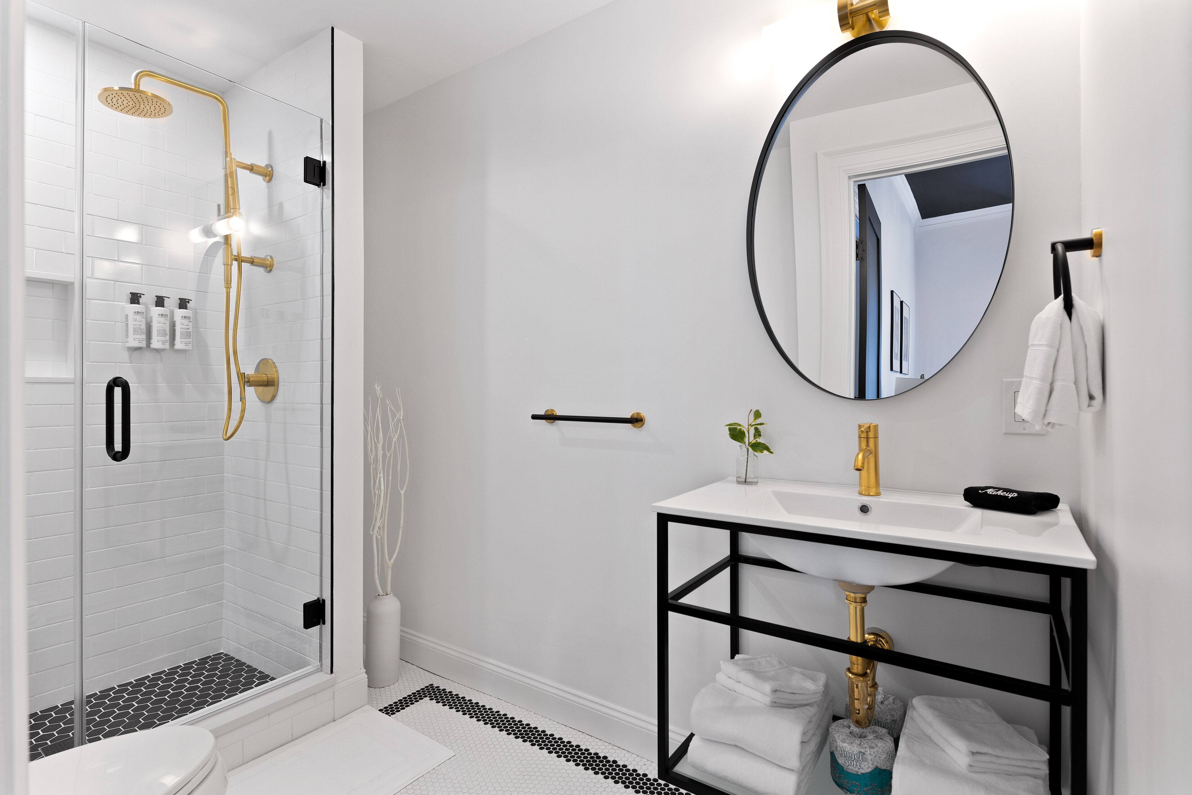 A modern bathroom with a glass-enclosed shower, a white sink with a black frame, and a round mirror.