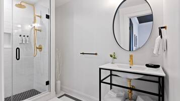 A modern bathroom with a glass-enclosed shower, a white sink with a black frame, and a round mirror.