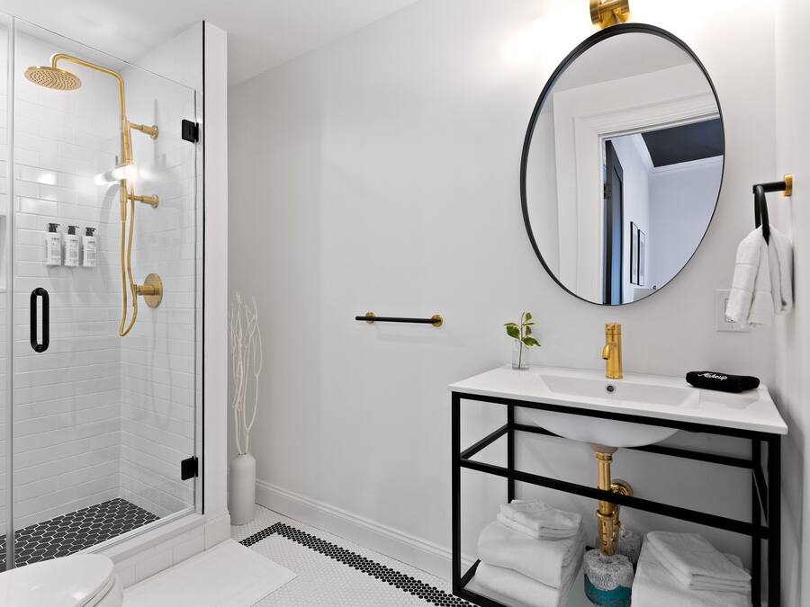 A modern bathroom with a glass-enclosed shower, a white sink with a black frame, and a round mirror.