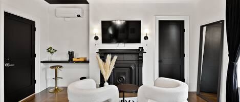Une chambre d’hôtel moderne aux couleurs noir et blanc, dotée d’une cheminée, d’un téléviseur à écran plat, d’un canapé et d’une petite table.
