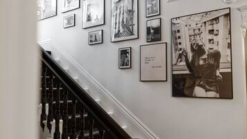 A staircase with a black handrail and white balusters, leading to a landing with a wall adorned with framed black and white photographs and a quote by Bob Dylan.
