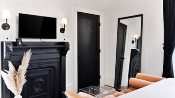 Una habitación de hotel moderna con una chimenea negra, un televisor de pantalla plana, un espejo grande y una cama con cubrecama blanco.