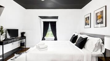 A modern hotel room with a large bed, a flat-screen TV, a desk, and a window with curtains.