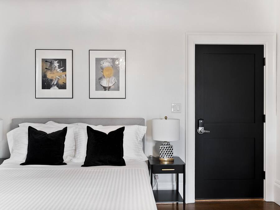 Un dormitorio ordenado con una cama, dos mesitas de noche, una puerta negra y dos cuadros en la pared.