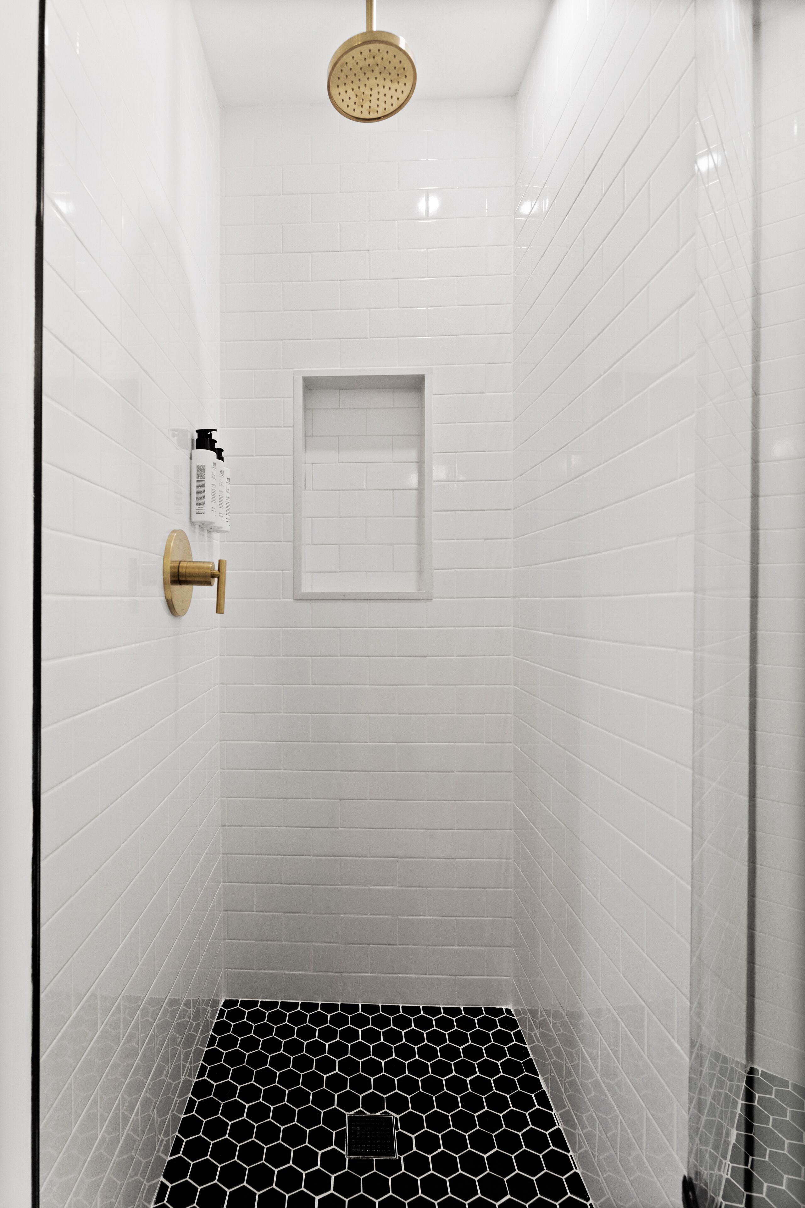 A modern shower with white tiled walls and a black and white patterned floor.