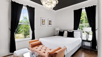 A modern bedroom with a large bed, a sofa, a side table, and a chandelier.