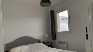 Makuuhuoneessa on sänky, yöpöytä, lamppu, ikkuna, jossa on verhot, ja patteri.