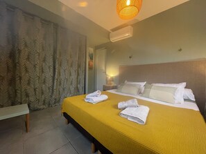 Una habitación de hotel con una cama, una lámpara de noche, un equipo de aire acondicionado y una ventana con cortinas.