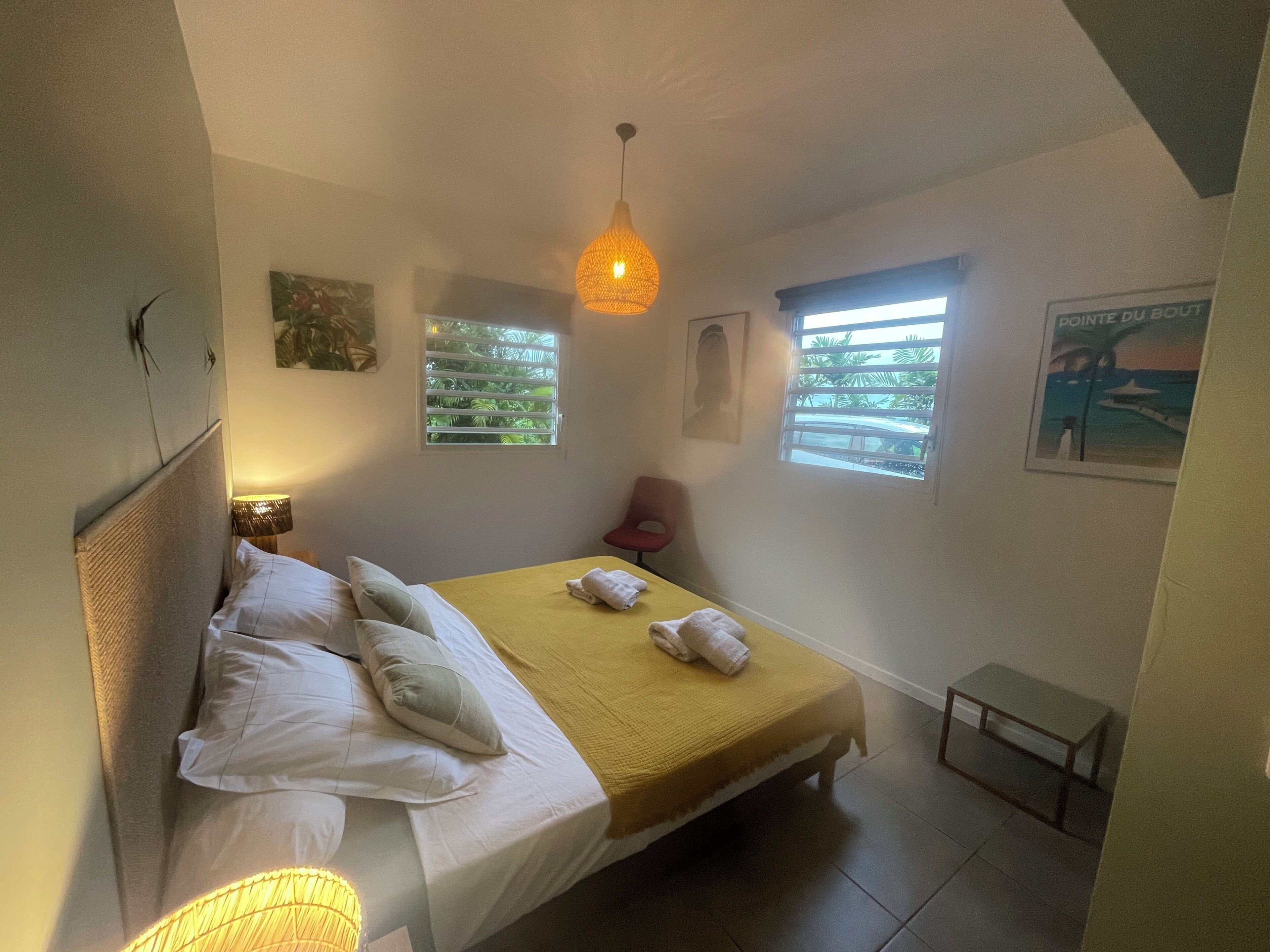 Un dormitorio con cama, mesita de noche, lámpara, ventana y un cartel en la pared.