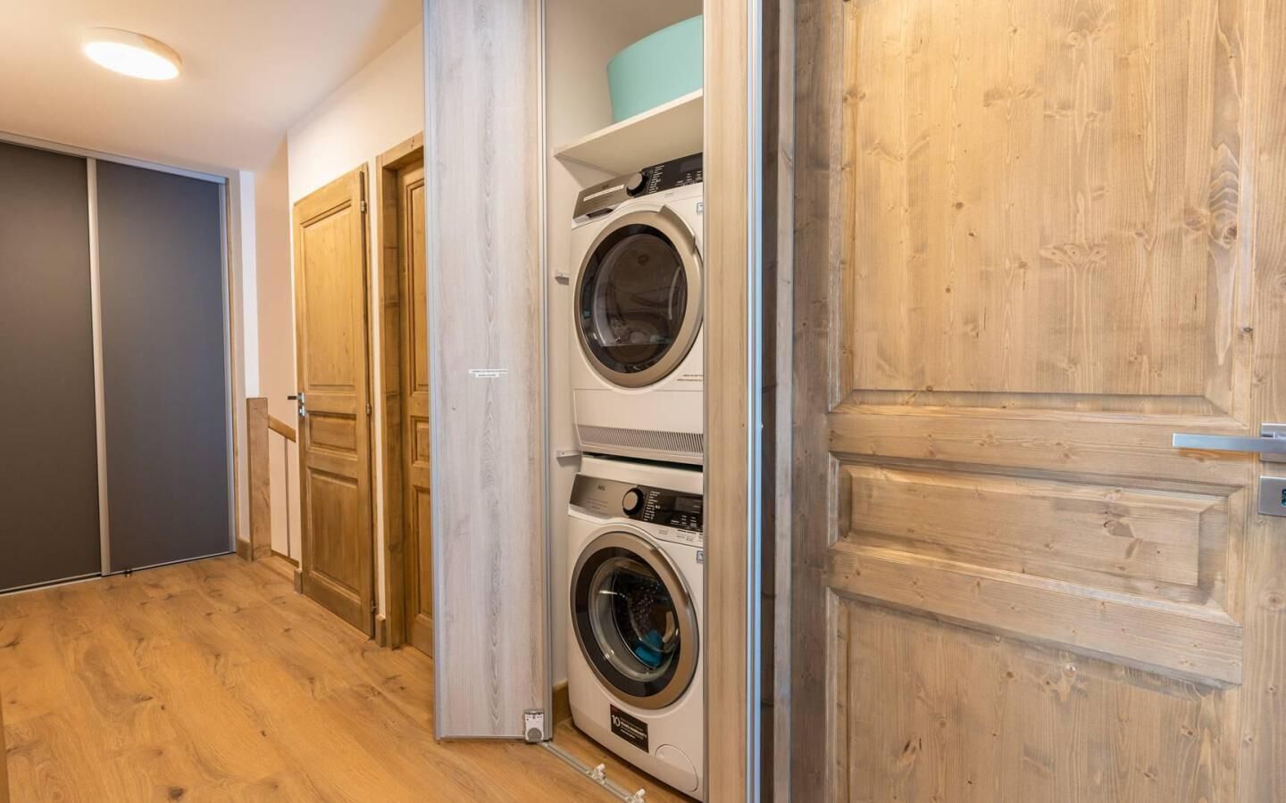A laundry room with two stacked washing machines, wooden doors, and a wooden floor.