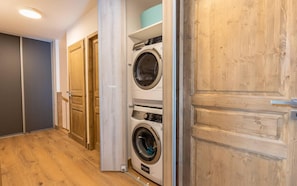A laundry room with two stacked washing machines, wooden doors, and a wooden floor.