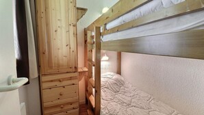Ein Stockbett mit Holzschrank und Schubladen, ein Fenster mit Vorhang und eine Nachttischlampe.