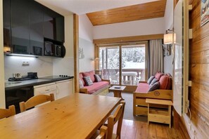 A compact kitchen with modern appliances, a dining area with a wooden table, and a cozy seating area with a sofa and a small table.