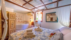 A bedroom with a large bed, a bathroom with a bathtub, and a ceiling with a wooden framework. - Blue East (Montemarcello)
