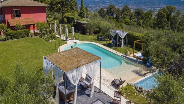 A private pool with a wooden deck, a covered seating area, and a view of the surrounding landscape. - Blue East (Montemarcello)