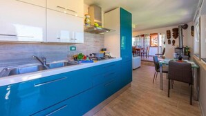 A modern kitchen with blue cabinets, a stainless steel sink, and a dining area with a table and chairs. - Blue East (Montemarcello)