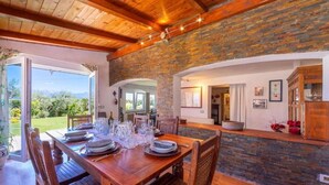 A dining area with a wooden table set for six, a stone wall, and a view of the outdoors. - Blue East (Montemarcello)