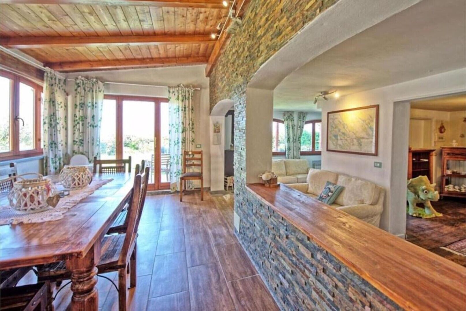 A spacious dining area with a wooden table and chairs, a stone wall, and a cozy living area with a sofa and a dinosaur toy.