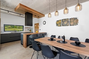 A modern kitchen with a large window, a dining area with a wooden table and chairs, and a kitchen island. - Luxury Villa Mojito with Pool (Labin)
