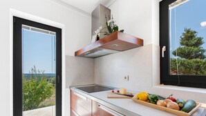 Une cuisine moderne dotée d’une grande fenêtre, d’une cuisinière encastrée et d’un plan de travail en bois sur lequel sont disposés des légumes frais.