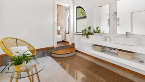 Une salle de bain moderne avec un meuble-lavabo blanc, deux vasques, un grand miroir et une chaise jaune agrémentée d’une plante en pot.