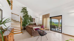 Un vaste espace de vie comprenant un escalier, un canapé, une table basse et une vue sur une terrasse extérieure, accessible par une porte vitrée.