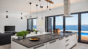 Ett modernt kök med en stor köksö, en matplats med en soffa och utsikt över havet.