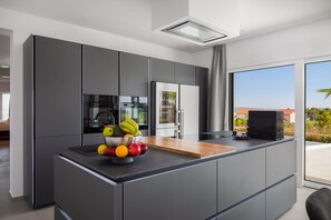 Une cuisine moderne dotée d’un îlot central, d’appareils électroménagers intégrés et d’une grande fenêtre offrant une vue sur l’extérieur.