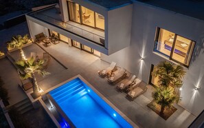 Une maison moderne à deux étages, dotée d’une piscine, d’un espace salon extérieur et de grandes fenêtres.