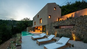 Uma casa moderna com parede de pedra e piscina. Há espreguiçadeiras e um bar visíveis.