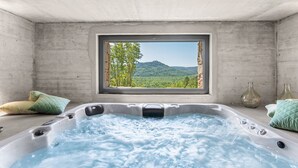 Uma banheira de hidromassagem com vista para uma encosta arborizada através de uma janela.