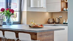 Une cuisine moderne avec un îlot central, des chaises blanches, un vase rempli de fleurs et une table à manger dressée avec une assiette de nourriture et un verre de vin.