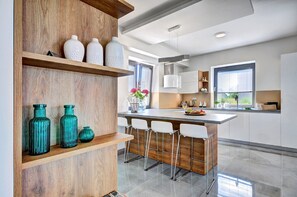Une cuisine moderne avec des étagères en bois, des tabourets de bar et une grande fenêtre.