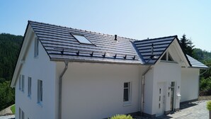 Een modern huis met twee verdiepingen, een schuin dak, meerdere ramen en een kleine tuin.