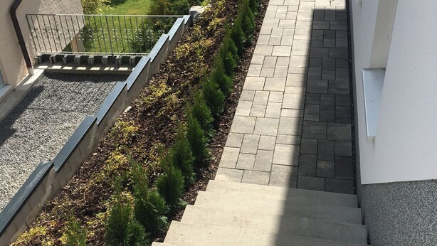 Een trap die leidt naar een woongebied met een tuin en een verhard pad.